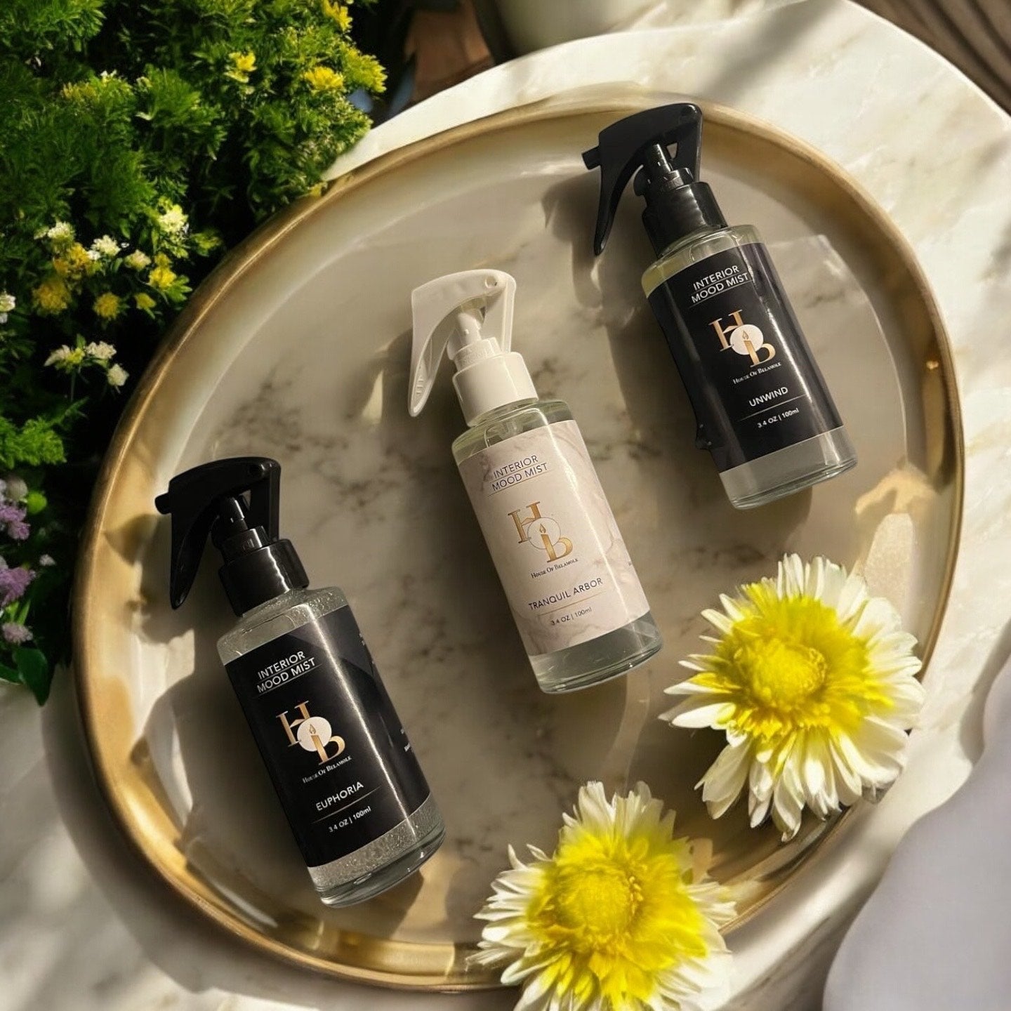Collection of luxury room mists with fruity, floral, woody, and spicy scent notes — including cherry, rose, sandalwood, and cinnamon — styled on an elegant home table surrounded by flowers to promote calming relaxation and natural home fragrance rituals.
